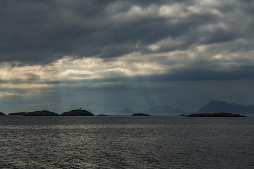 Norwegian seascape, rocky coast with dramatic skies, the sun breaks through the clouds, sheer cliffs, small islands illuminated by the sun. High quality photo