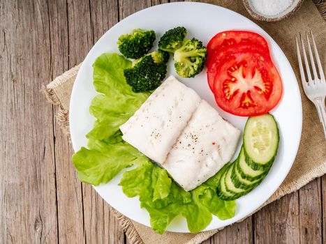 Steamed cod fish. Paleo, keto, fodmap healthy diet with vegetables on white plate on wooden table, top view