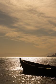 A wooden boat near the seashore in the orange rays of sunset against the background of clouds and sky haze symbolizes tranquility and tranquility. A small piece of rocky shore is visible on the horizon. The sky takes up most of the frame