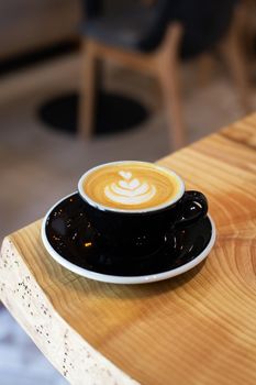 Black cup of coffee with cream, cappuccino with a pattern close-up stands on a wooden table.