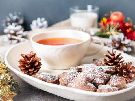 Christmas or new year card. Winter holiday composition, side view, selective focus, blue, gray background. Cup of tea, cookies, fir cones, candles, gift