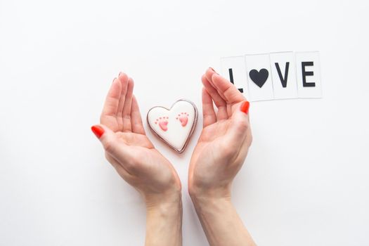 Beautiful children's footprint in the shape of a heart, the girl's hands hug the heart. Love lettering