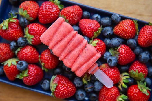 Delicious ice cream from fresh strawberries and blueberries close-up lies on fresh strawberries and blueberries. Assorted background