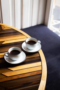 Two modern cups of espresso on a wooden table, a table in front of the window. Coffee break
