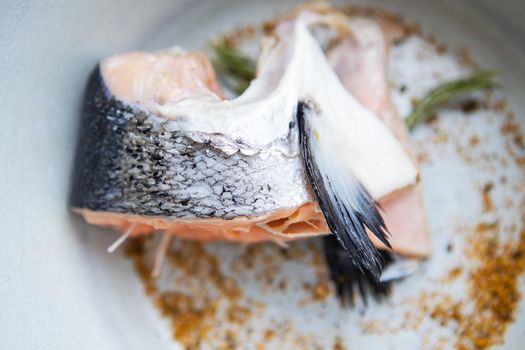 A chopped piece of salmon steak is on a plate along with spices and rosemary. Cooking process