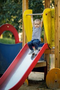 Little boy is ready to skate from the playground slides. Cheerful little boy having fun while sliding outdoors.