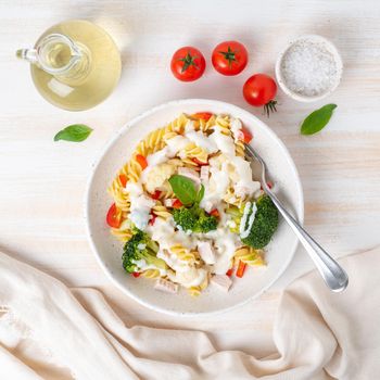 Pasta fusilli with vegetables, boiled steamed meat, white sauce on white wooden table, low-calorie food, low-fat diet, top view.