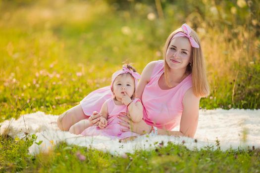 mother and daughter in identical pink dresses are sitting in nature