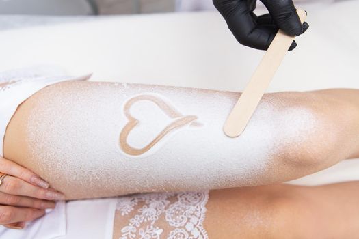 Professional cosmetology, body epilation, leg hair removal concepts. Shugaring, laser hair removal. Legs of a client in cream with a heart on her leg