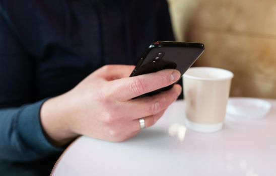 Paper coffee cup, smartphone in male hand. Coffee to go, walks in the fresh air. Student, remote study