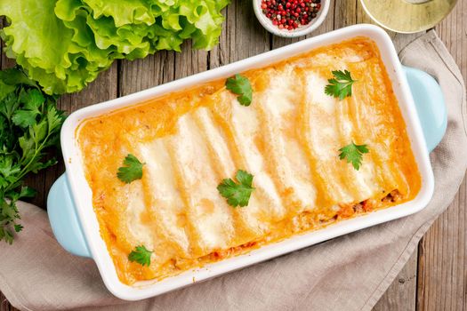 Cannelloni with filling of ground beef, tomatoes, baked with bechamel tomato sauce, top view, old dark wooden background