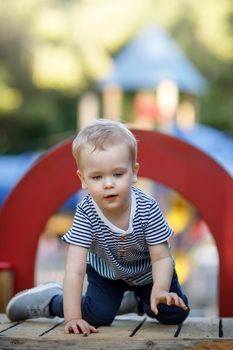 Cute 3-year-old boy plays on a playground in a hot sunny day and concentrates to get through a red arch.