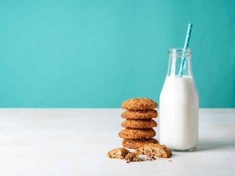Oatmeal cookies with flax seeds and milk in bottle, healthy snack. Light background, bright blue wall.