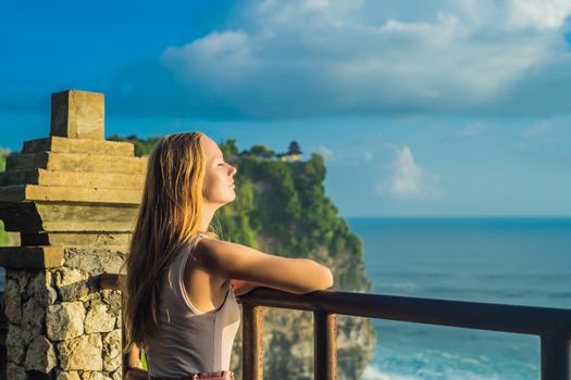 Young woman traveler in Pura Luhur Uluwatu temple, Bali, Indonesia. Amazing landscape - cliff with blue sky and sea.