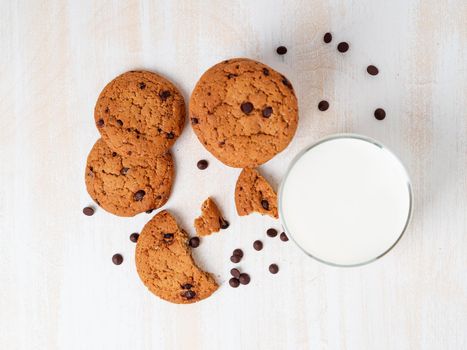 Oatmeal cookies with chocolate drops and milk in glass, healthy snack. Light background, white wooden table, top view.