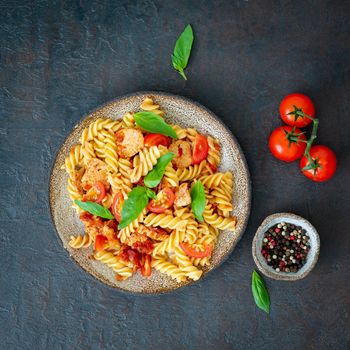 fusilli pasta with tomato sauce, chicken fillet with basil leaves on dark stone concrete background, top view.