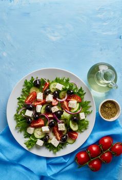 Greek salad on white plate on bright blue table, top view, copy space