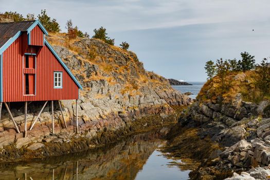 Lonely small fishing house of red color on the coast on Lofoten Islands, classic norwegian landscape, rocky coast with dramatic sky. High quality photo