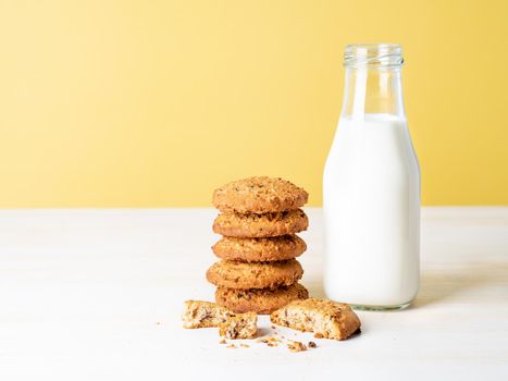 Oatmeal cookies with flax seeds and milk in bottle, healthy snack. Light background, bright yellow wall.
