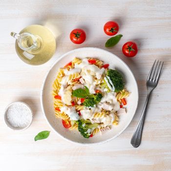 Pasta fusilli with vegetables, boiled steamed meat, white sauce on white wooden table, low-calorie diet, low-fat food, top view.