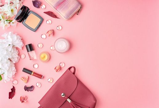 Flat lay woman accessories with cosmetic, facial cream, bag, flowers on bright pink table. Copy space