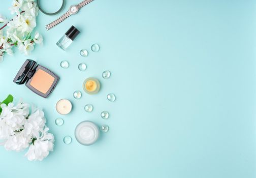 Flat lay woman accessories with cosmetic, facial cream, bag, flowers on pastel blue table. Copy space