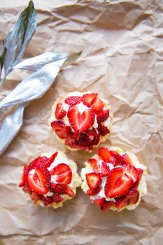 Beautiful cupcakes with strawberries along with a branch on kraft paper.