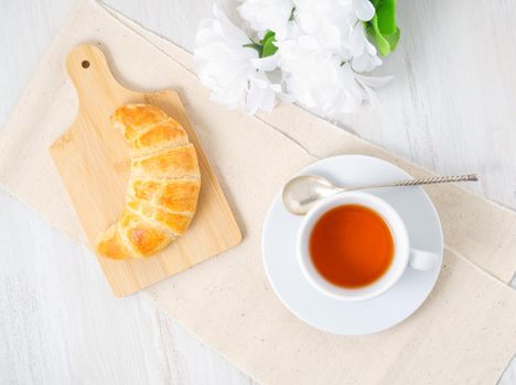 Cup of tea, flowers and a fresh baked puff pastry on a white table. Delicious croissants on wooden board, top view