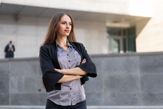 Business woman with long hair dressed black jacket standing outdoor near corporate office building hand folded Beautiful caucasian female business person portrait city street Side view looking away