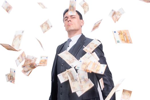 Proud male millionaire in formal wear looking at camera while standing under falling bunch of money isolated on white background