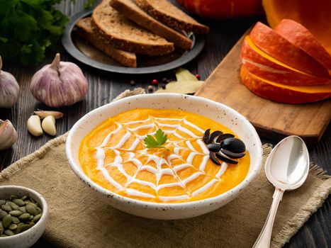 Funny food for Halloween. Pumpkin puree soup, spider web, dark old wooden table, a side view.