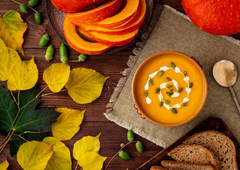 Autumn food. Pumpkin puree soup, leaves, a dark brown old wooden table, top view.
