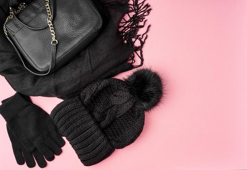 Flat lay winter or autumn warm woman accessories - black knitted scarf, hat, bag on bright pink background, copy space.