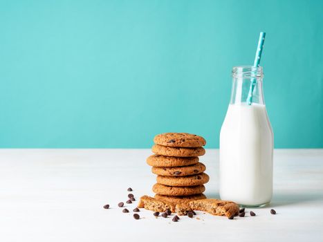 Oatmeal cookies with chocolate drops and milk in bottle, healthy snack. Light background, bright blue wall.