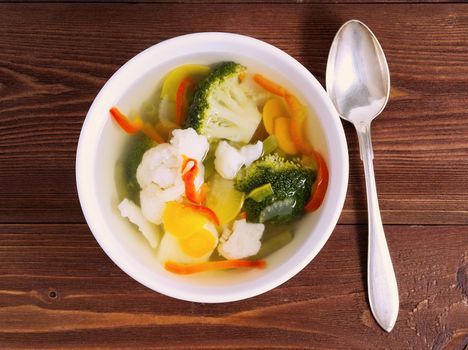 Bright dietary vegetarian soup with cauliflower, broccoli and other vegetable on a brown wooden background, top view.
