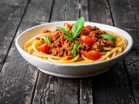 pasta bolognese with tomato sauce, ground minced beef, basil leaves on dark rustic wooden table, side view, close-up