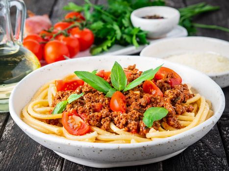 pasta bolognese with tomato sauce, ground minced beef, basil leaves on dark rustic wooden table, side view, close-up