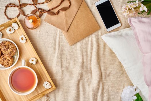 Mockup with women's accessories on bed tea, cookies, pillows, flowers, letter, notebook. Cozy home rest, vacation, weekend. Copy space. Cozy women's creative world.