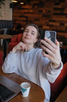 Smiling woman sitting on kitchen sofa talking by videocall dating online looking at phone. Video blogger vlogger recording vlog at home. Lifestyle vlogging concept, head shot portrait