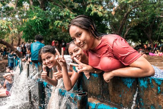 Group of Latin girls posing for the camera making the gesture of peace with their hands and fingers, smiling enjoying summer in the waters of a dam in a river in Villa El Carmen, Nicaragua.