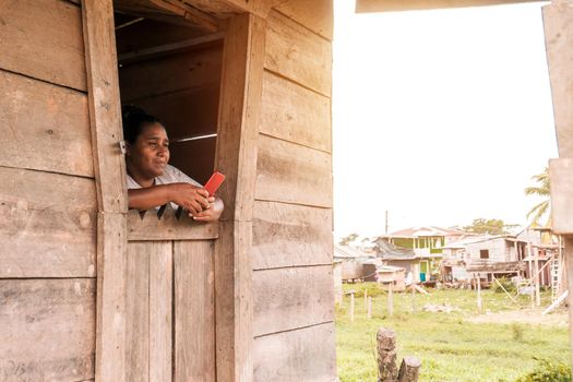 Mestizo woman inside her wooden house in a rural community in the Caribbean of Nicaragua using her cell phone to surf the internet.