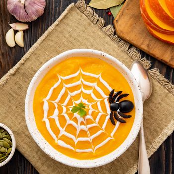 Funny food for Halloween. Pumpkin puree soup, spider web, dark old wooden table, a top view.