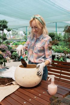 Young woman planting a bush in flower pot using dirt in garden center