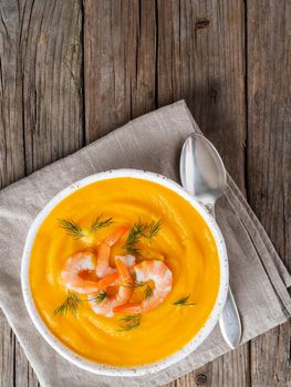 Delicious yellow pumpkin cream soup with shrimp on dark gray old rustic wooden table, top view, copy space, vertical.