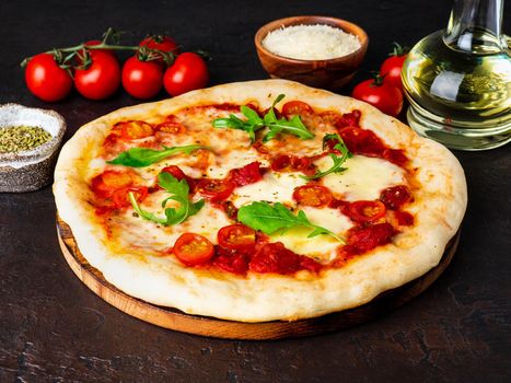 hot homemade Italian pizza margherita with mozzarella and tomatoes on dark brown stone table, side view.