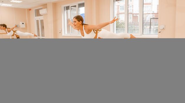 Group of young womans fitness instructor in Sportswear Leggings and Tops, stretching in the gym before pilates, on a yoga mat near the large window on a sunny day, female fitness yoga routine concept.