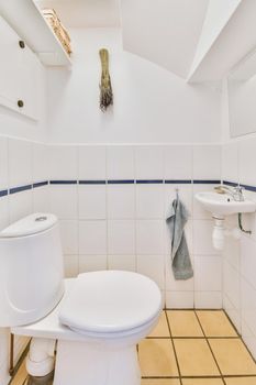 Ceramic toilet and small sink with towel under mirror in corner in lavatory room with beige tile