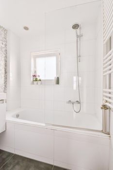 Bathtub with glass shower placed in corner near sink and mirror in small light bathroom with white tile walls