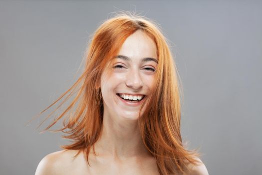 Beautiful dark burnt orange windy hair girl smiling. Studio portrait with happy face expression against gray background.