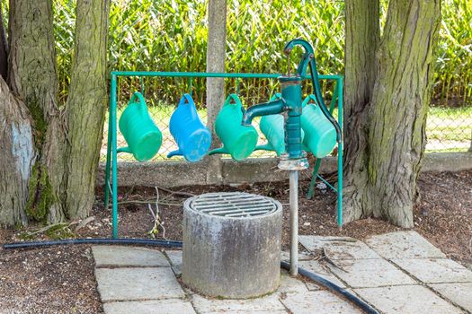 Watering cans hanging next to an old water pump at municipal cemetery. Handful gardening equipment at graveyard to take care for grave greenery
